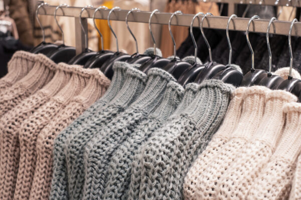 Multicolored knitted sweaters hanging on hangers in a clothing store close up.